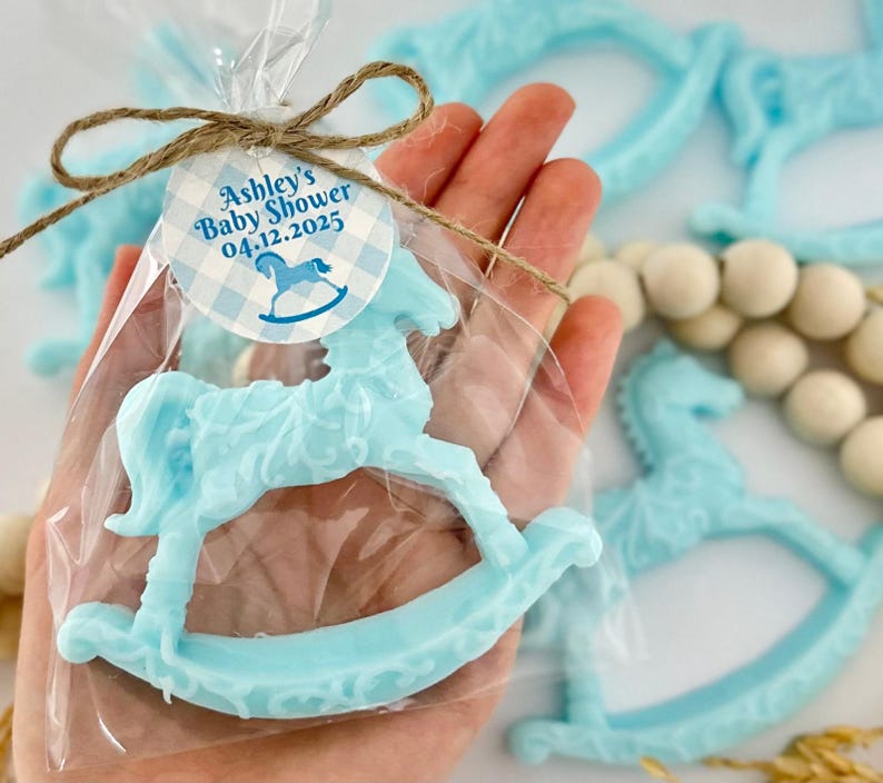 Może przedstawiać: Niebieskie mydło w kształcie konika na biegunach z biało-niebieską kratką z napisem "Ashley's Baby Shower 04.12.2025".