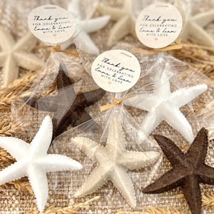 May include: Thank you for celebrating Emma & Lian with love.  A set of five small, white, brown, and beige starfish favors in clear cellophane bags tied with twine.