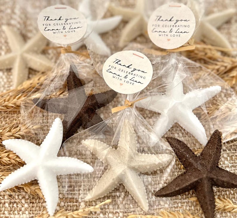 May include: Thank you for celebrating Emma & Lian with love.  A set of five small, white, brown, and beige starfish favors in clear cellophane bags tied with twine.