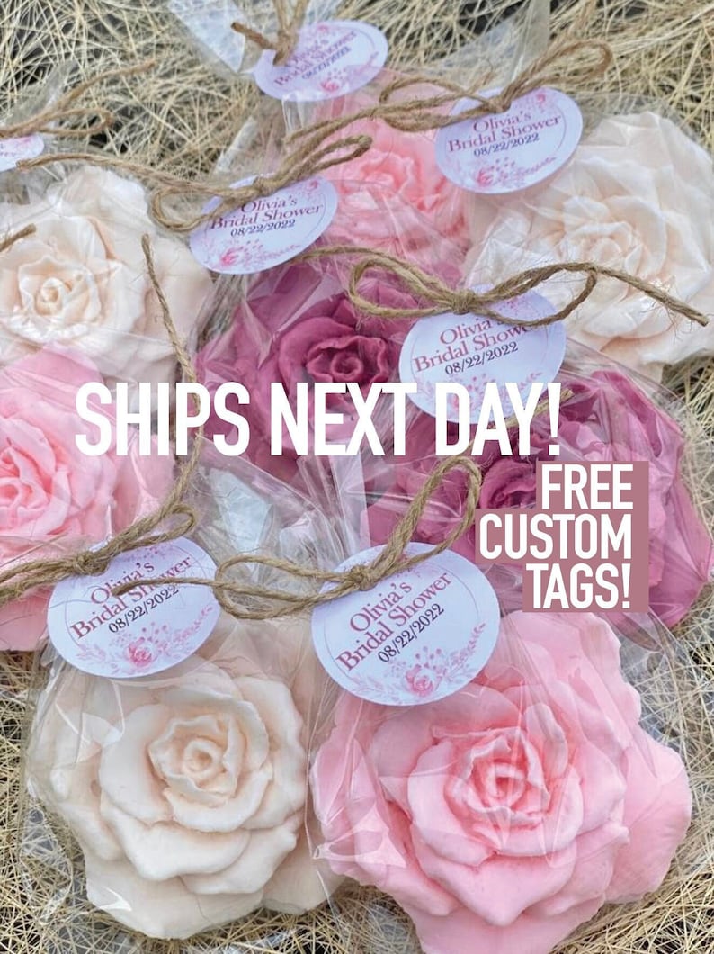 Puede incluir: Un conjunto de seis jabones en forma de rosa rosa y blanco envueltos en bolsas de celof&aacute;n transparentes con lazos de cuerda. Cada jab&oacute;n tiene una etiqueta redonda blanca con el texto "Olivia's Bridal Shower 08/22/2022". El texto "SHIPS NEXT DAY! FREE CUSTOM TAGS!" se superpone a la imagen.