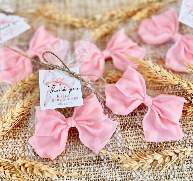 May include: Pink satin bows tied with twine and packaged in clear cellophane bags. Each bag includes a small thank you tag with the text "Thank you Kayla's Baby Shower 08/12/24".