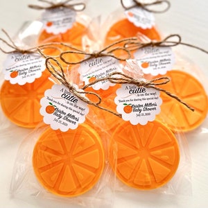 May include: Orange-scented soap favors wrapped in clear cellophane bags with a white tag that reads "A little cutie is on the way! Thank you for sharing this special day! Kristen Miller's Baby Shower July 25, 2020".