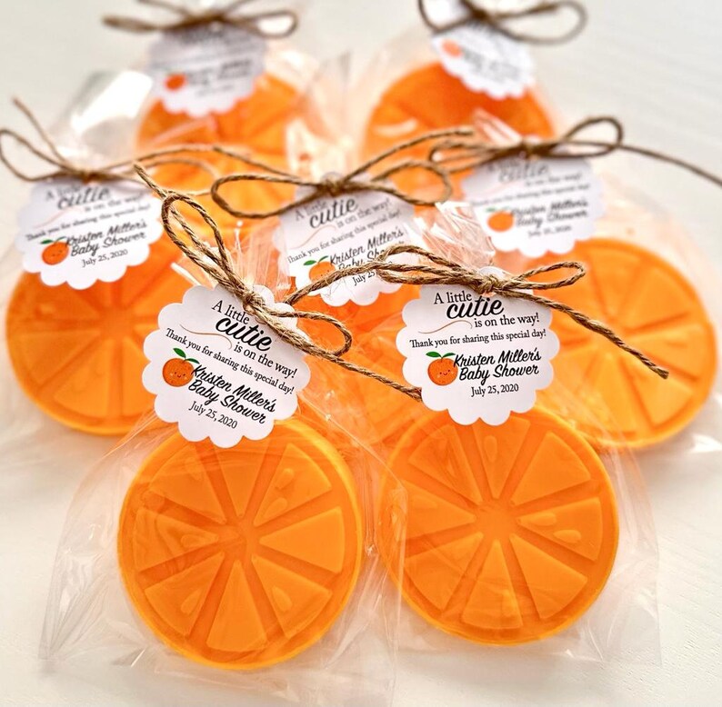 May include: Orange-scented soap favors wrapped in clear cellophane bags with a white tag that reads "A little cutie is on the way! Thank you for sharing this special day! Kristen Miller's Baby Shower July 25, 2020".