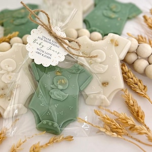May include: Baby shower favors shaped like baby onesies in sage green and off-white, with a duck design. Each onesie is individually wrapped and tied with twine and a tag that reads "Thank you for showering Baby Jones with love - Amy & John."