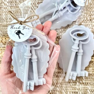 May include: Two gray, vintage-style key shaped soaps wrapped in clear cellophane bags with a thank you tag. The tag has a black and white illustration of keys and the words "Thank You".