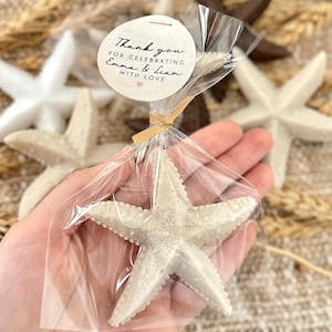 May include: A white starfish wrapped in clear cellophane with a brown ribbon and a round tag that says "Thank you for celebrating Emma & Liam with love".