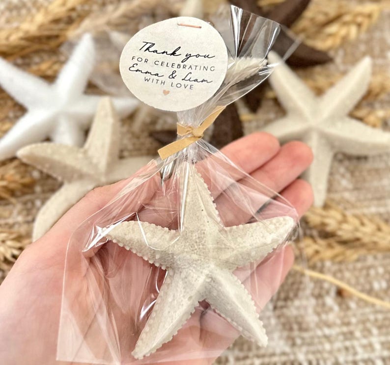 May include: A white starfish wrapped in clear cellophane with a brown ribbon and a round tag that says "Thank you for celebrating Emma & Liam with love".