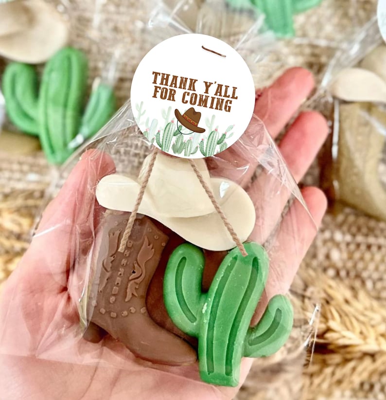 May include: A small gift bag filled with a brown cowboy boot, a green cactus, and a white cowboy hat. The bag has a round tag attached that says "Thank y'all for coming".