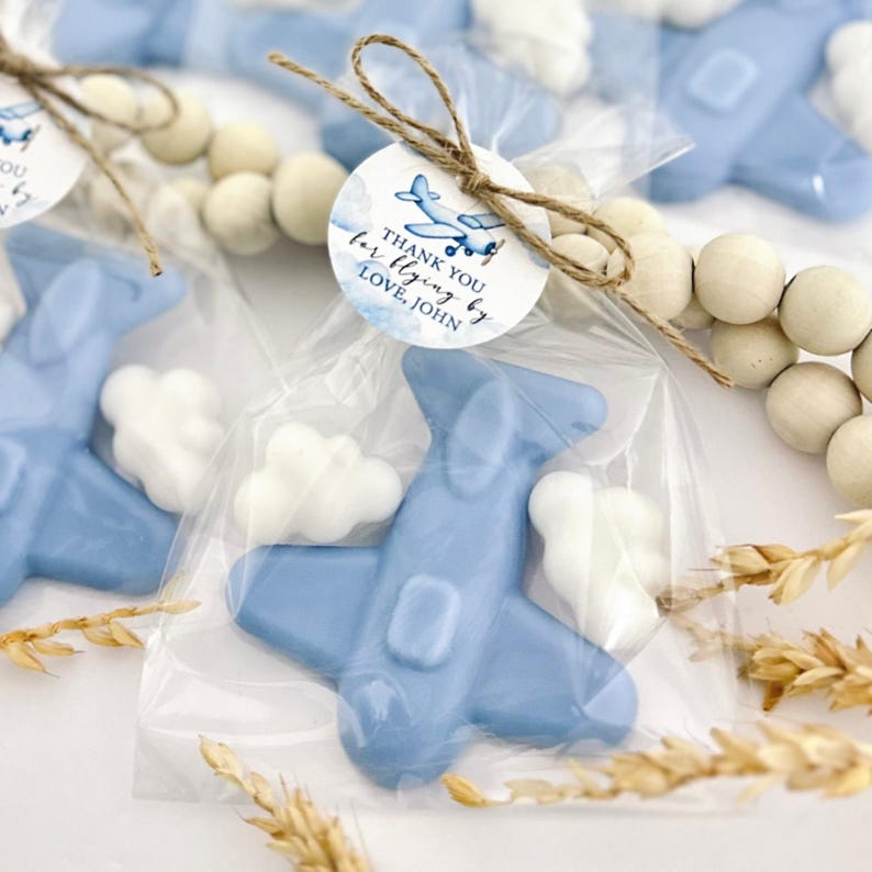 May include: Blue airplane shaped soap favors with white cloud accents, packaged in clear cellophane bags tied with twine and a round tag that reads "Thank you for flying by Love, John".