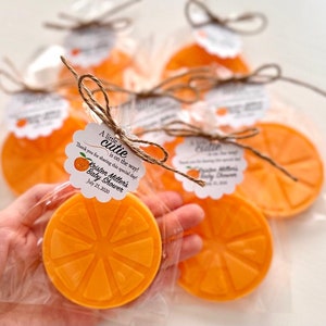 May include: Orange-scented soap favors wrapped in cellophane bags with a white tag that reads "A little cutie is on the way! Thank you for sharing this special day! Kristen Miller's Baby Shower July 25, 2020"