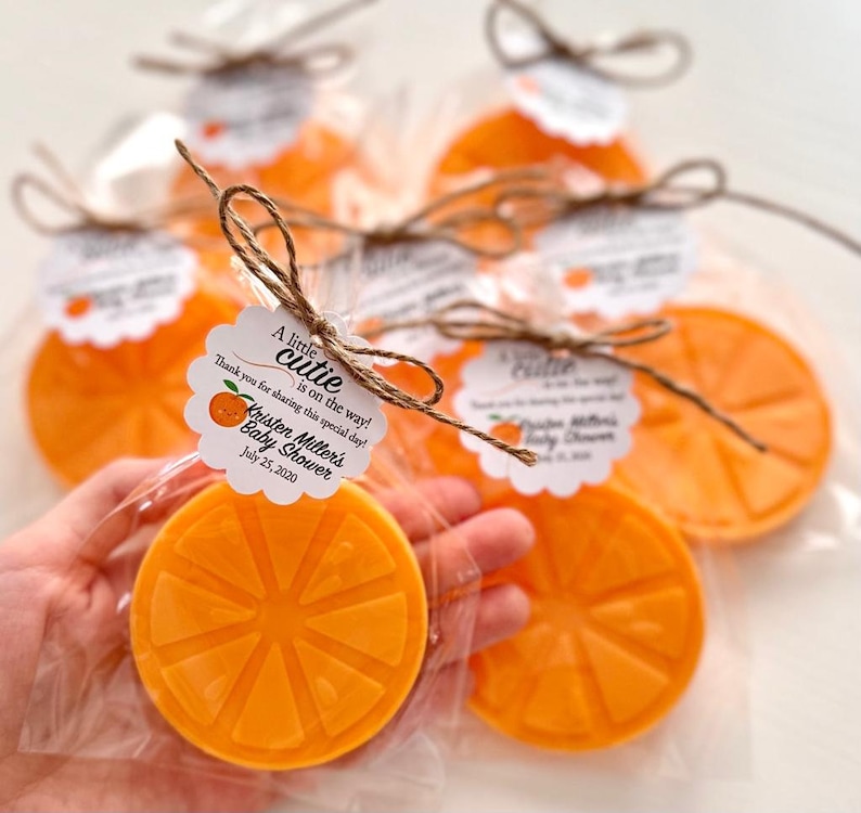 May include: Orange-scented soap favors wrapped in cellophane bags with a white tag that reads "A little cutie is on the way! Thank you for sharing this special day! Kristen Miller's Baby Shower July 25, 2020"
