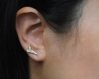 May include: A gold leaf-shaped earring with a delicate design. The earring is worn in the upper cartilage of the ear.
