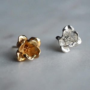 May include: Two flower-shaped earrings, one gold and one silver. Both earrings feature a textured surface and a raised centre.