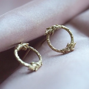 May include: A pair of gold-toned earrings with a circular design featuring a leafy pattern.