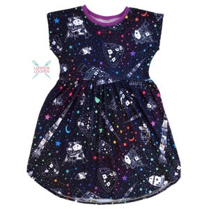 May include: A black and purple short-sleeved dress with a space-themed print featuring rockets, stars, and the moon. The print is in rainbow colors.