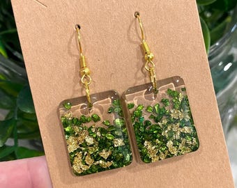 May include: A pair of gold square dangle earrings with green and gold glitter embedded in clear resin.