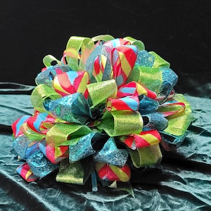 May include: A large, colorful bow made of green, blue, and pink ribbon. The bow is made of multiple layers of ribbon, and the ends of the ribbon are curled.