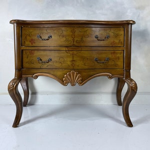 May include: A two-drawer wooden side table with ornate carvings and painted floral designs. The table has a curved top and cabriole legs.