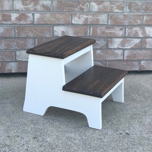May include: A white two-step stool with a dark brown wood top. The stool is made of wood and has a simple design.