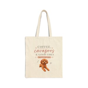 May include: Cream-colored tote bag with the words "COFFEE, cavapoos & GOOD VIBES" in a pink script. A brown cavapoo dog illustration is below the text. The bag has two handles.