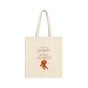 May include: Cream-colored tote bag with the text "Less People, More Cavapoos" in a decorative font. A brown Cavapoo puppy illustration is below the text. The bag has two handles and is made of a canvas-like material.