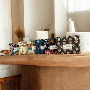 May include: Six rectangular fabric pouches arranged in a row, each featuring a unique floral or geometric pattern and a white rectangular label reading ATELIER DU CHAT QUI PIQUE. The pouches vary in colour, including navy, green, and cream tones.