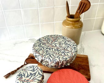 Puede incluir: Tres cubiertas de tela reutilizables para cuencos con bordes elásticos. Una cubierta grande presenta un fondo gris oscuro con un patrón de hojas de color verde claro y rosa. Se incluyen una cubierta pequeña a juego y una cubierta de color terracota sólido.