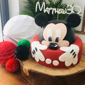 Puede incluir: Un pastel de Mickey Mouse rojo y negro con glaseado blanco y una decoraci&oacute;n que dice "Matthew 30".