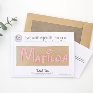 K&ouml;nnte beinhalten: Eine wei&szlig;e rechteckige Karte mit dem Text Handmade especially for you und Thank You for supporting my small business, mit einem mittigen Ausschnitt, der einen rosa B&uuml;geltransfer mit dem Namen Matilda und einen braunen Umschlag zeigt.