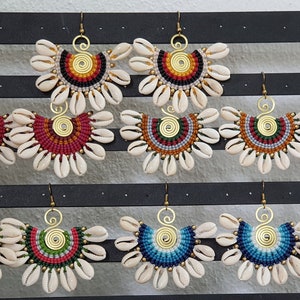 May include: A collection of handmade earrings displayed on a black holder. Each earring features a fan-shaped design made with seashells, colorful beads, and a gold-toned spiral center. The earrings come in various color combinations.