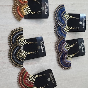 May include: A collection of handmade earrings in various colors, including orange, blue, black, and red. Each earring features a fan-shaped design with intricate macrame detailing and gold-colored metal accents. The earrings are displayed on black cards with the word "Fashion".