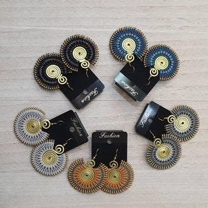 May include: A collection of handmade earrings in various colors, including blue, black, white, and orange. Each pair features a circular design with a spiral center and a gold-colored hook. The earrings are displayed on black cards with the word "Fashion".