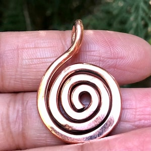 May include: A copper-colored pendant with a spiral design. The pendant is made of a single piece of metal, with a loop at the top for a chain. The spiral starts at the center and expands outwards.