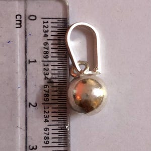 May include: A silver earring featuring a spherical charm. The earring, including the hook, is approximately 2 cm long. The charm is a smooth, round ball. The earring is shown next to a ruler for scale.