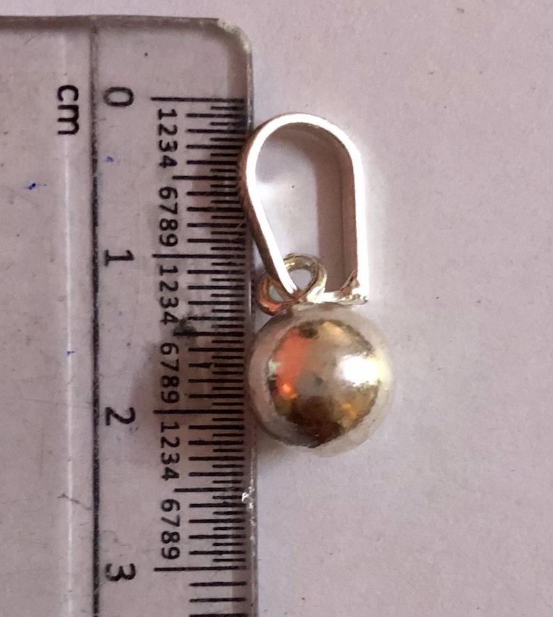 May include: A silver earring featuring a spherical charm. The earring, including the hook, is approximately 2 cm long. The charm is a smooth, round ball. The earring is shown next to a ruler for scale.