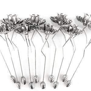 May include: A set of 12 silver metal candle holders shaped like flowers with a small cone-shaped base. The holders are designed to hold tea lights or votive candles.