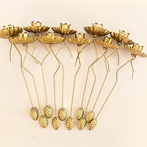May include: Set of ten gold metal candle holders with a floral design. Each holder has a long, thin stem with a pine cone-shaped base.