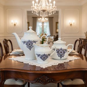 May include: A formal dining table set with a white and blue floral patterned tea set. The tea set includes a teapot, creamer, and covered sugar bowl. The table is made of dark wood and is set with plates and silverware.
