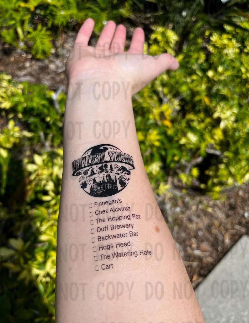 K&ouml;nnte beinhalten: Ein schwarzes und wei&szlig;es tempor&auml;res Tattoo mit dem Universal Studios Logo und einer Liste von Restaurants und Bars, darunter Finnegan's, Chez Alcatraz, The Hopping Pot, Duff Brewery, Backwater Bar, Hogs Head, The Watering Hole und Cart.