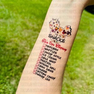 May include: A white Mickey Mouse head with a red border and the text "I'm Just Here For The Snacks" inside. Below the Mickey Mouse head is a list of snacks with checkboxes next to each item. The list includes popcorn, waffles, candy apple, ice cream, dole whip, pretzel, spring roll, corn dogs, churro, cotton candy, and turkey leg. The text "Gia's 5th Birthday" is written in red above the list.