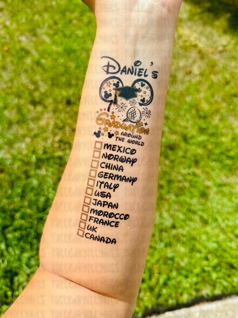May include: A temporary tattoo with a graduation theme. It features a Mickey Mouse ear design with a graduation cap and the text "Daniel's Graduation Around the World". Below the design is a list of countries with checkboxes: Mexico, Norway, China, Germany, Italy, USA, Japan, Morocco, France, UK, Canada.