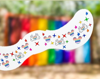 Könnte beinhalten: Ein weißes, gebogenes Dekorationselement mit bunten Mickey-Mouse-Kopf-Designs, Handgesten und Sternformen. Die Designs enthalten Regenbogenfarben, die den LGBTQ+-Stolz symbolisieren. Der Hintergrund ist ein verschwommener Regenbogenverlauf.