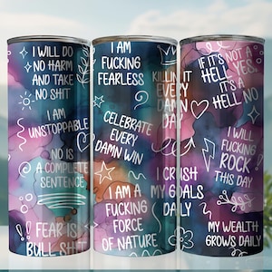 May include: Three stainless steel tumblers with colorful watercolor backgrounds and white motivational text. The text on the tumblers includes phrases like "I am fearless", "I will do no harm", and "I will fucking rock this day".