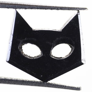 May include: Black cat-shaped charm with cut-out eyes, held by tweezers.