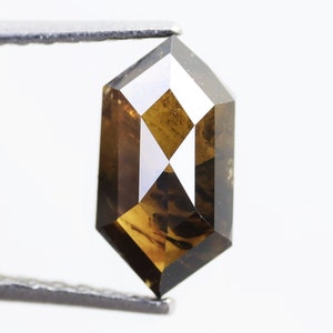 Op de afbeelding: Een bruine en zwarte, achtkantige diamant edelsteen vastgehouden door een pincet.
