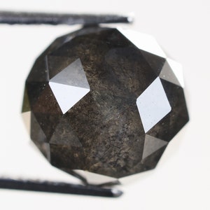 Könnte beinhalten: Ein schwarzer Diamant mit einer facettierten, runden Form. Der Diamant wird von einer Pinzette gehalten.