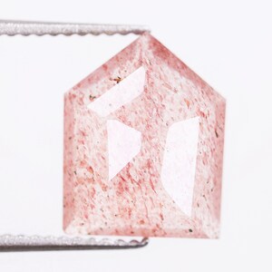 Puede incluir: Una piedra preciosa hexagonal rosa facetada con una superficie rugosa y texturizada.