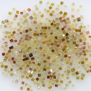 Può includere: Una grande collezione di piccoli diamanti quadrati sfaccettati in varie tonalità di giallo, marrone e trasparente. I diamanti sono sparsi su una superficie bianca.