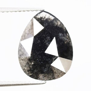 Puede incluir: Un diamante negro en forma de pera con un diseño facetado. El diamante tiene un color gris y negro con facetas blancas.