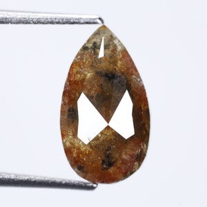 Pode incluir: Um diamante marrom em forma de pêra com inclusões, segurado por uma pinça contra um fundo branco.